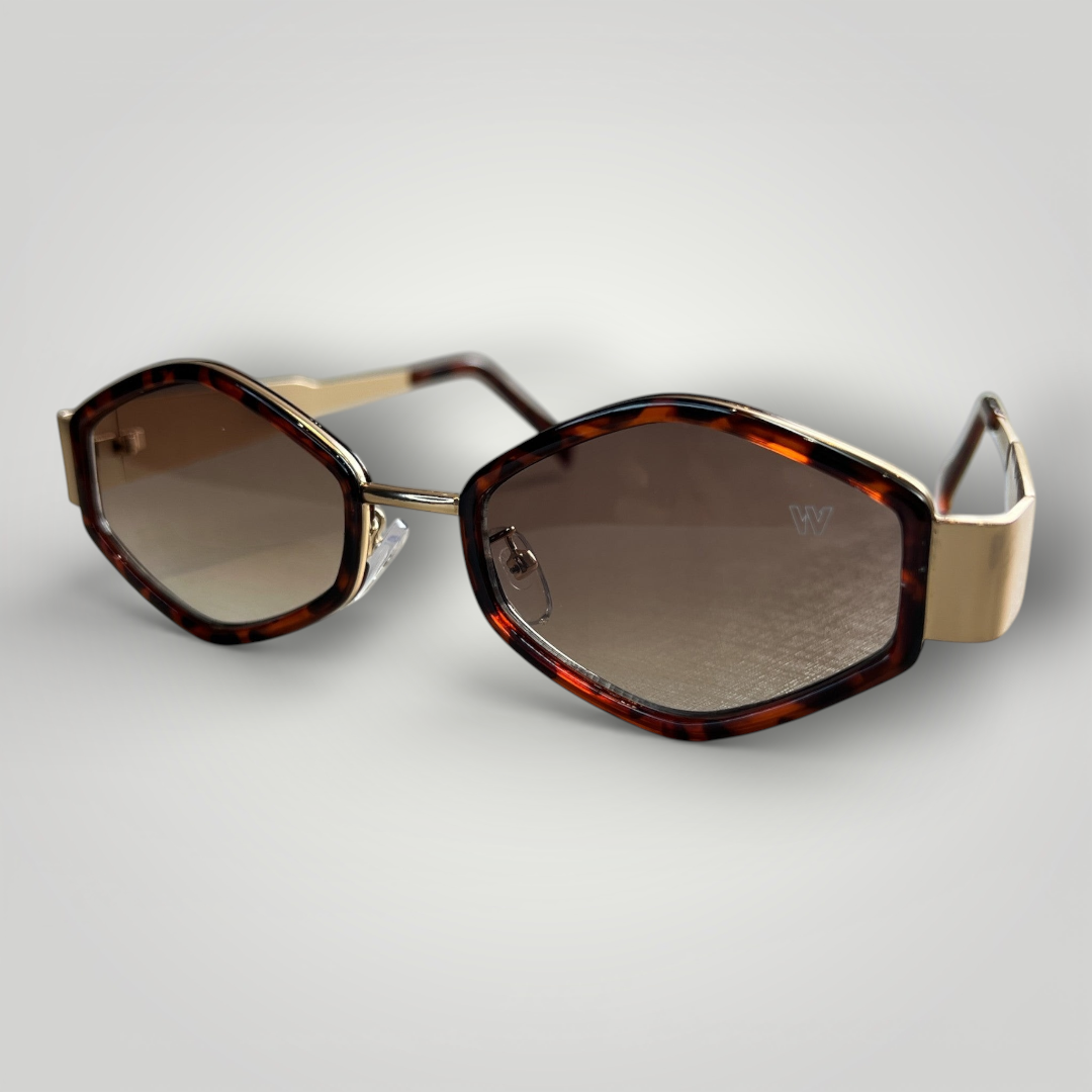 Óculos de sol W One formato Prisma camuflado marrom com hastes metálicas douradas e lentes marrons, um modelo que une personalidade e sofisticação em cada detalhe. O design diferenciado valoriza o olhar com elegância e presença marcante. No uso diário, a proteção UV400 garante conforto e segurança visual, equilibrando estilo contemporâneo e funcionalidade.