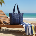 Bolsa tote puffer azul marinho W One Brand Store com bolsos externos e alças reforçadas sobre espreguiçadeira na praia.