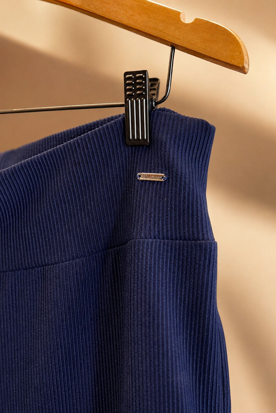 Detalhe do cós da calça pantalona W One Brand Store em tecido canelado azul marinho com placa metálica da marca