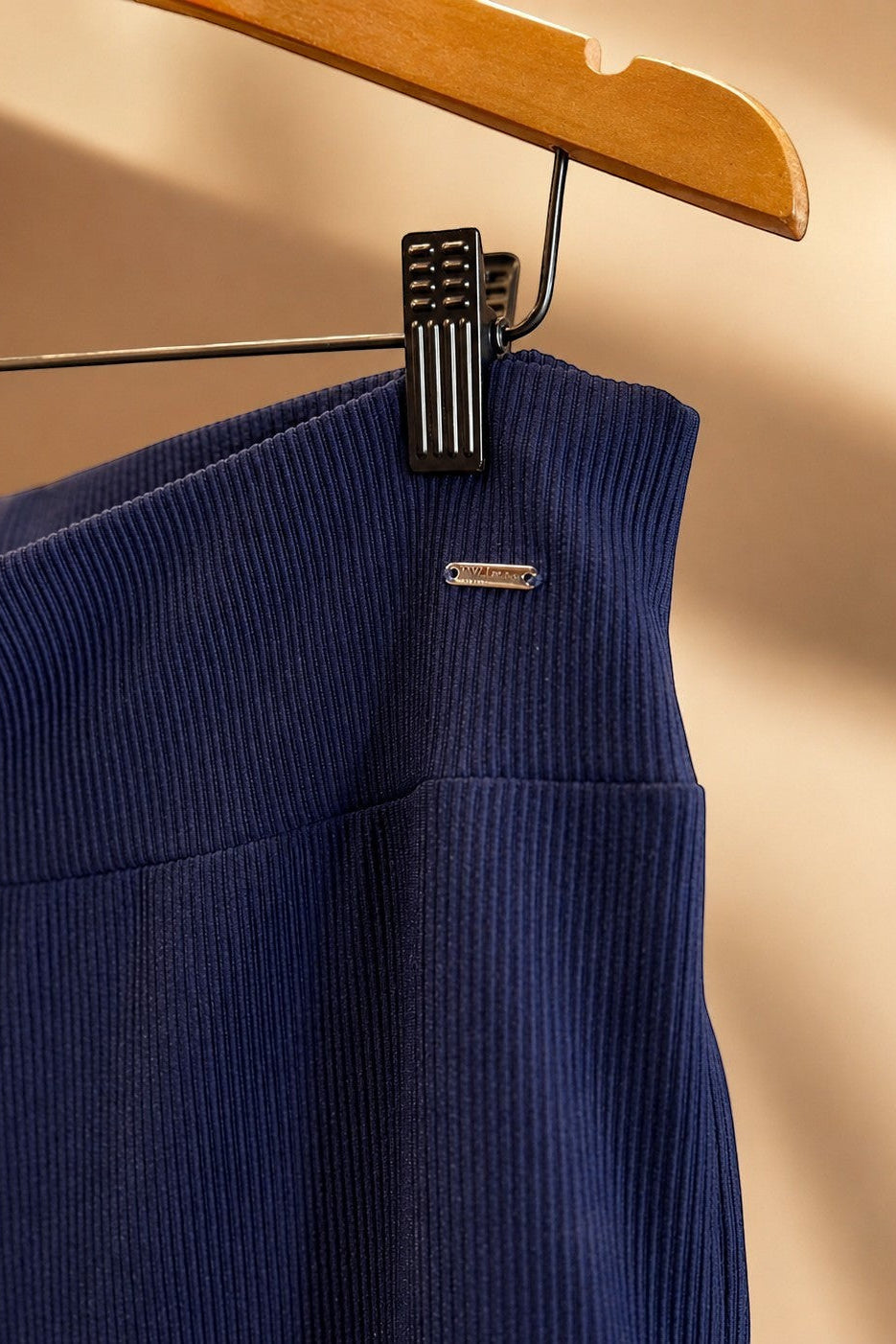 Detalhe do tecido canelado azul marinho da calça W One Brand Store com placa metálica da marca em cabide