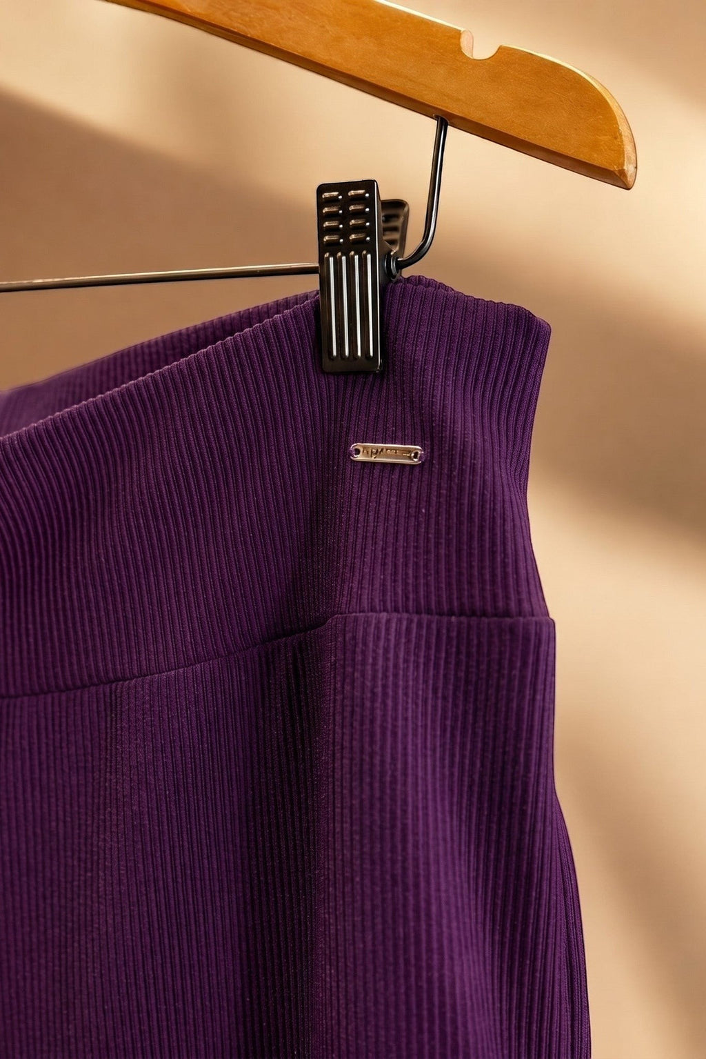 Detalhe do cós da calça pantalona W One Brand Store na cor vinho, em tecido canelado com placa metálica da marca.