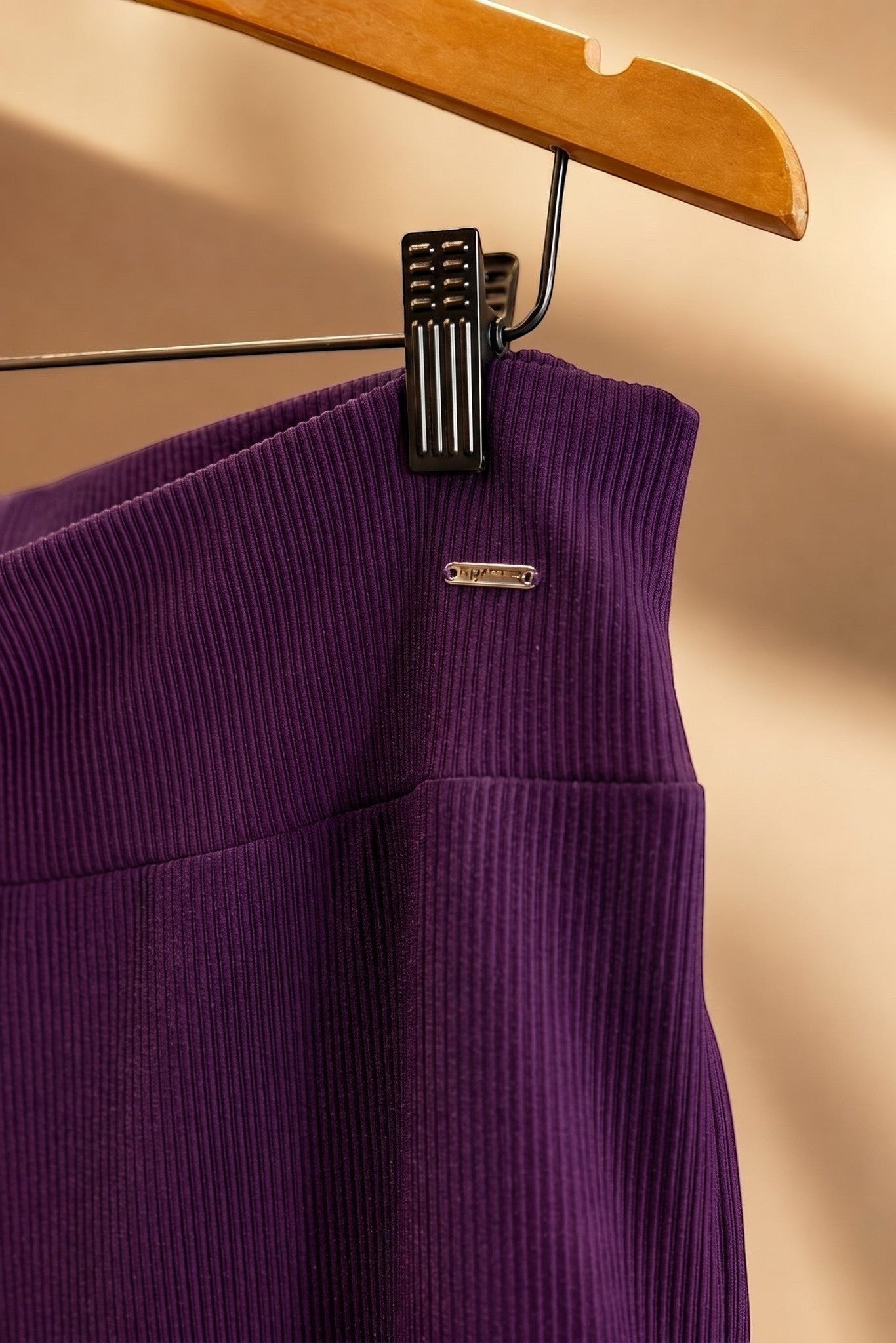 Detalhe do cós da calça pantalona W One Brand Store na cor vinho, em tecido canelado com placa metálica da marca.