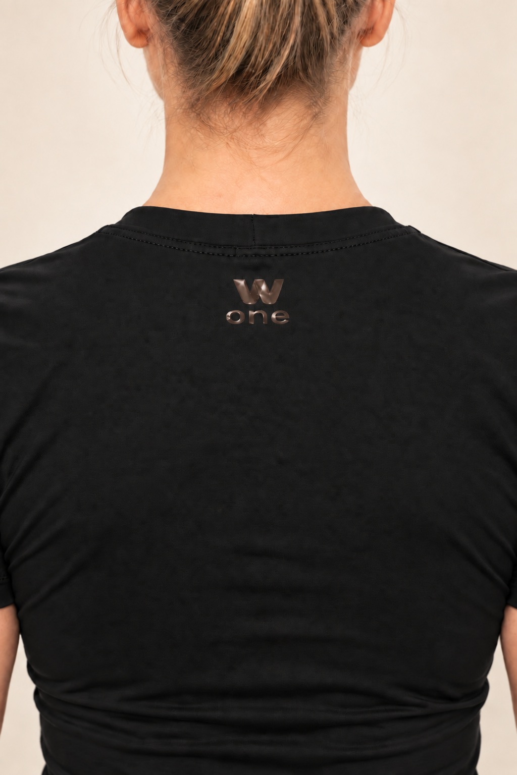 Detalhe das costas da camiseta cropped preta W One Brand Store com logo metalizado e tecido de poliamida