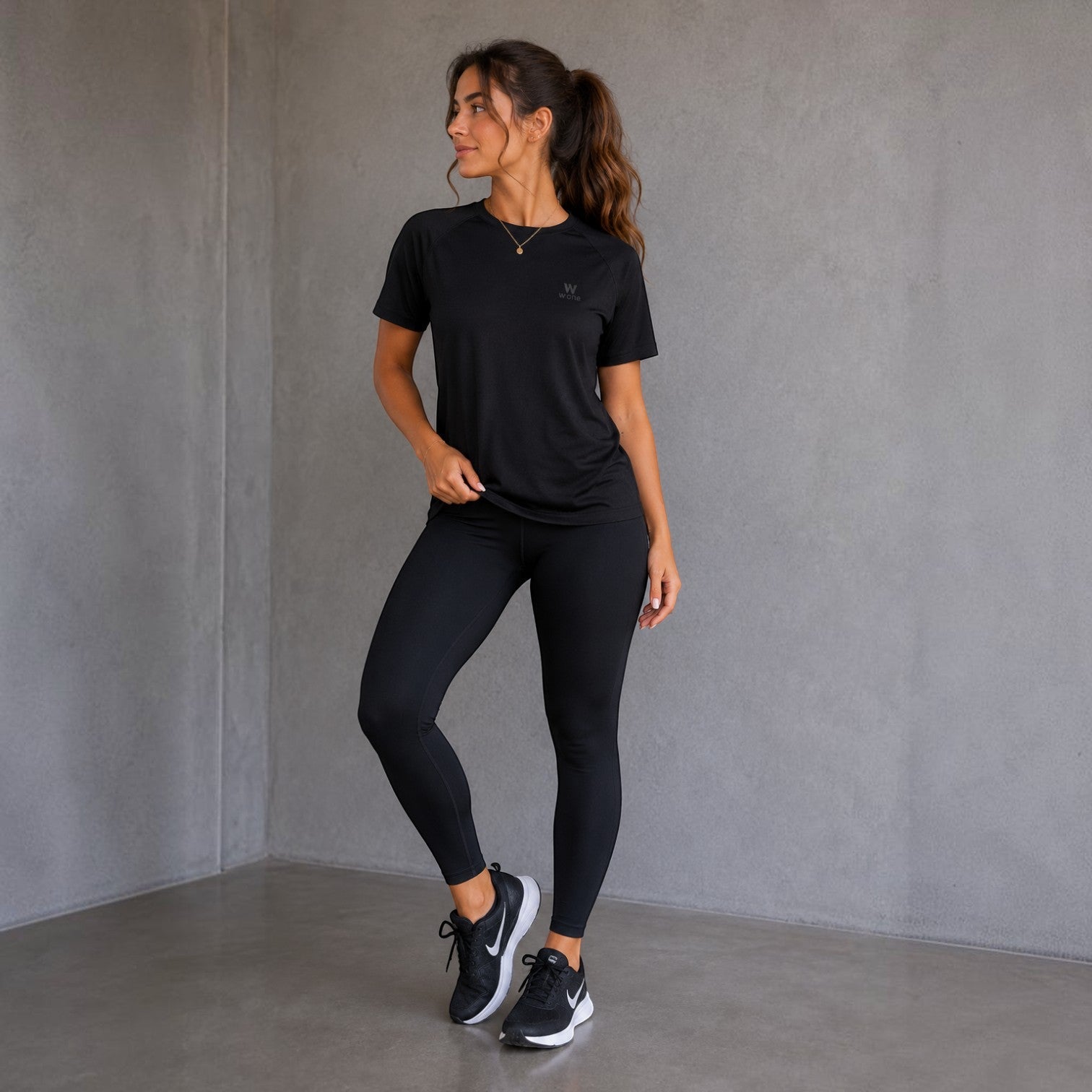 Mulher vestindo camiseta W One Brand Store preta raglan com legging combinando em ambiente cinza minimalista