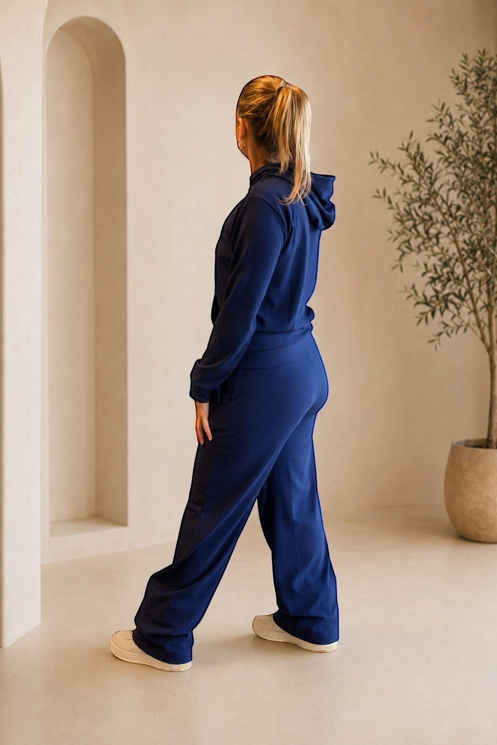 Modelo veste conjunto W One Brand Store azul marinho canelado com blusa de capuz e calça pantalona em ambiente neutro