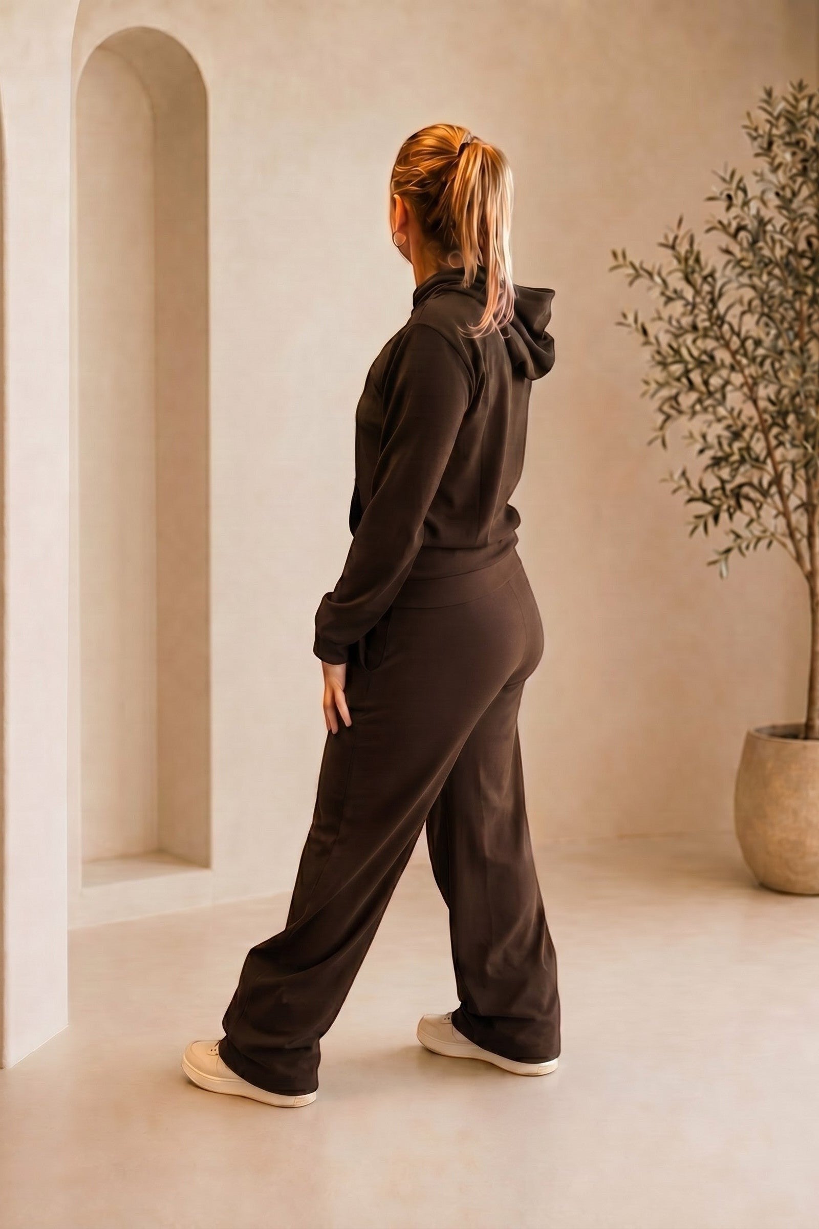 Modelo veste conjunto W One Brand Store cor café com blusa de capuz canelada e calça pantalona em ambiente neutro