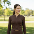 Modelo veste jaqueta cropped marrom W One Brand Store em tecido dry fit com zíper frontal em ambiente ao ar livre