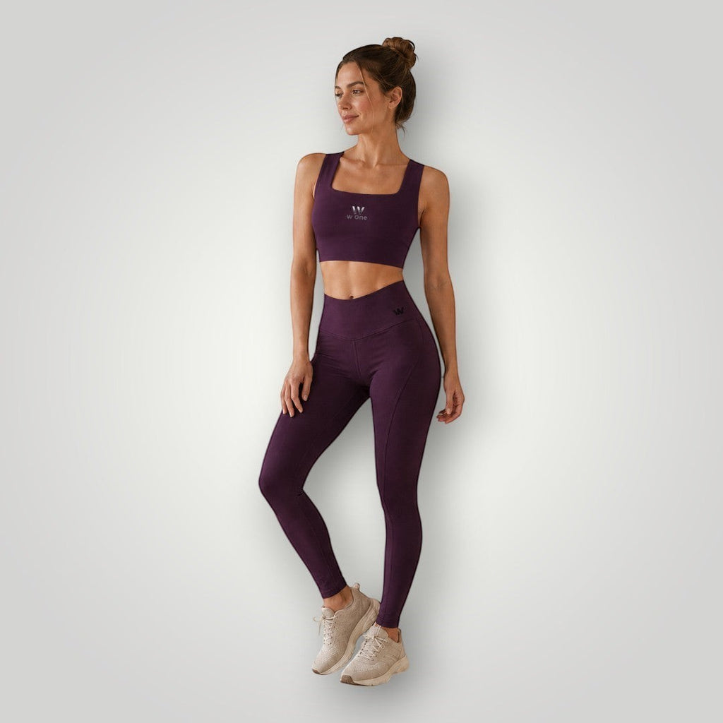 Modelo vestindo conjunto fitness W One Brand Store na cor vinho com legging de recortes e top de média compressão
