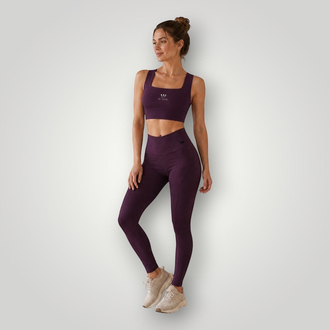 Modelo vestindo conjunto fitness W One Brand Store na cor vinho com legging de recortes e top de média compressão