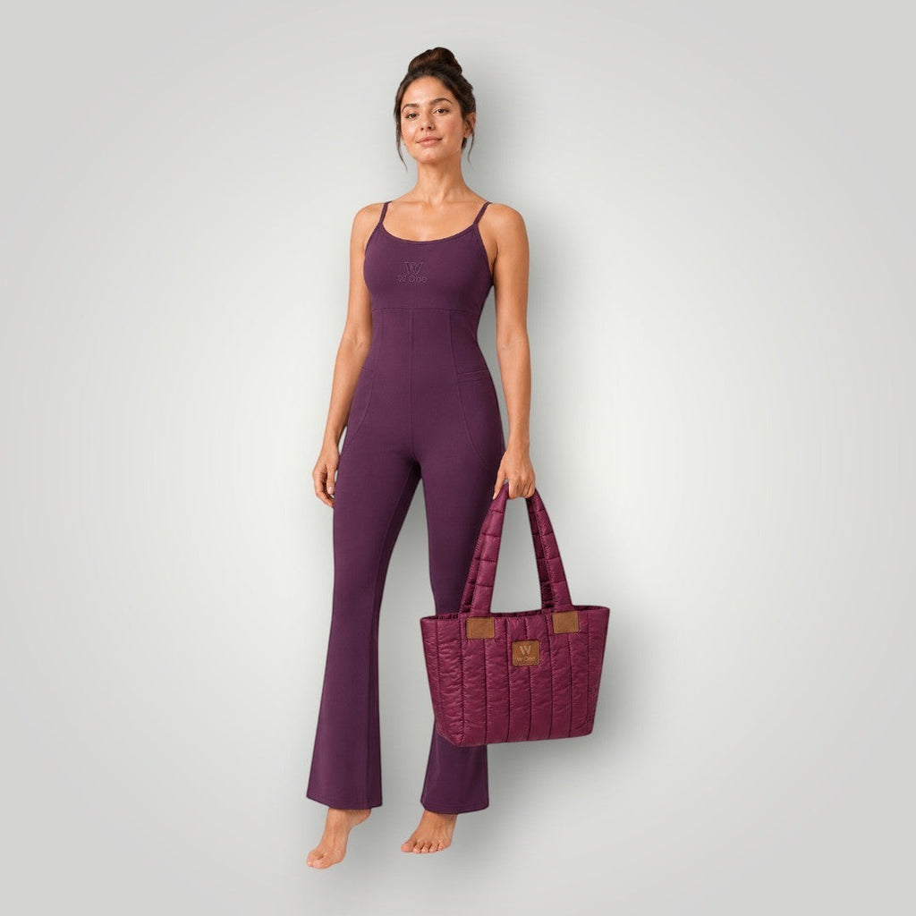 Modelo vestindo macacão W One Brand Store cor vinho com alças finas e bolsa acolchoada combinando em fundo cinza