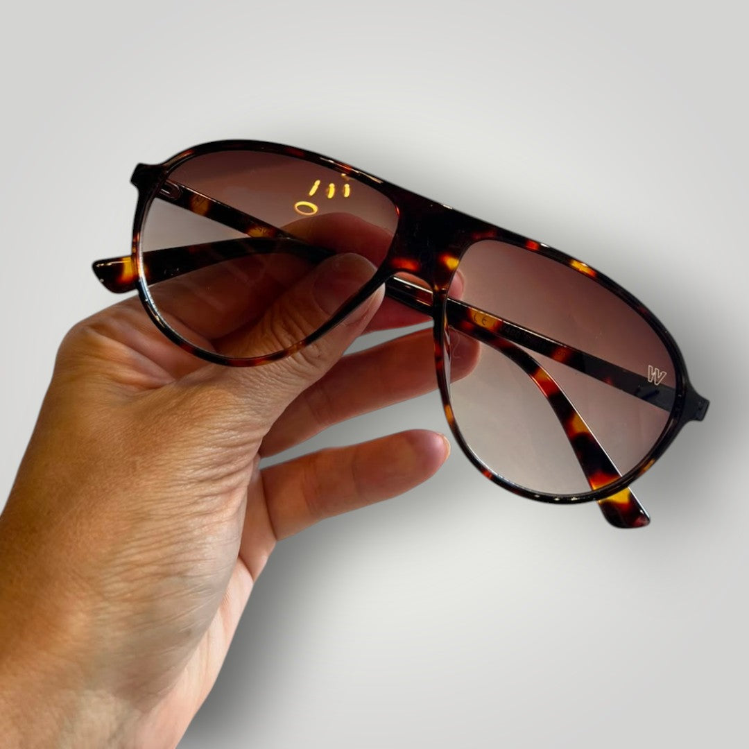 Óculos de sol aviador W One Brand Store com armação em acetato estampado e lentes marrons degradê segurados na mão