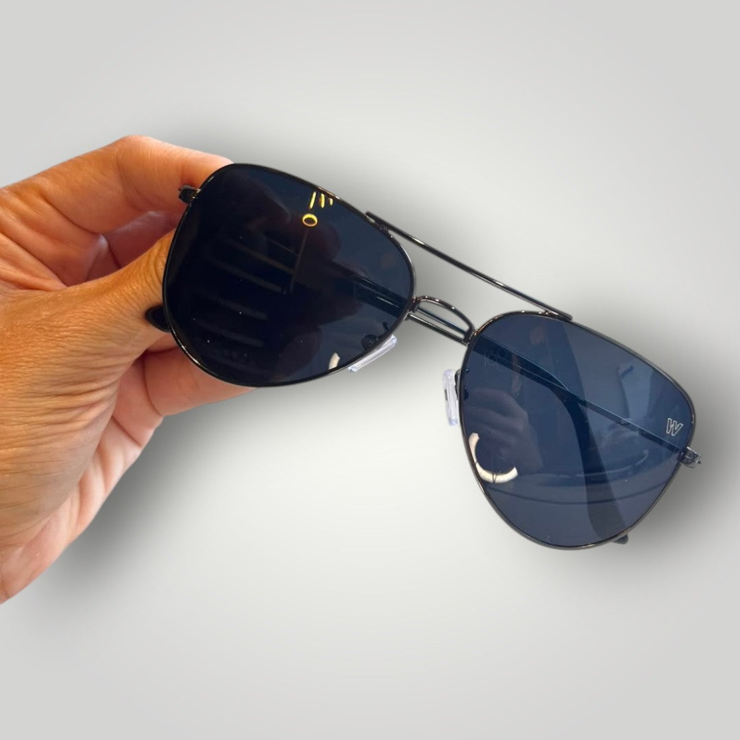 Óculos de sol aviador W One Brand Store com armação de metal preta e lentes fumê em mão humana