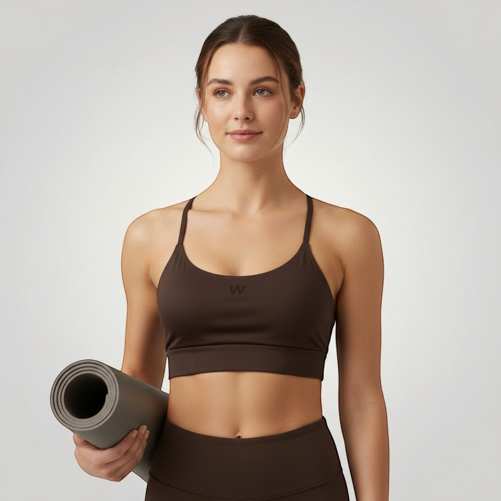 Modelo vestindo top esportivo marrom W One Brand Store com alças fixas e média sustentação, segurando tapete de yoga